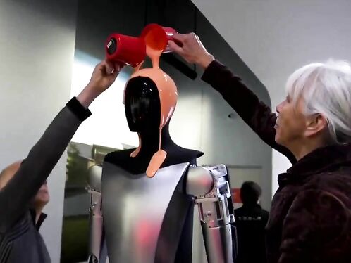 Two Elderly People With Intellectual Disabilities Are Wrapping A Tesla Optimus Car In Latex.