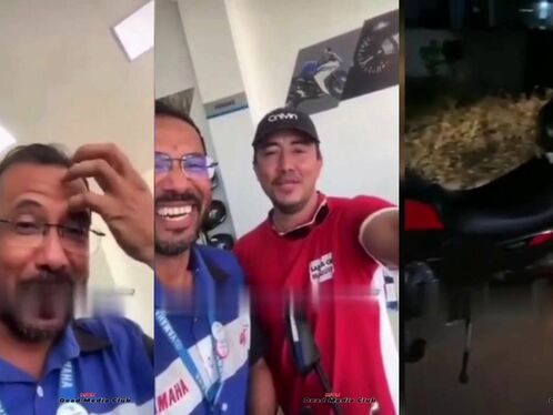 Men laugh while holding a motorbike in an indoor room